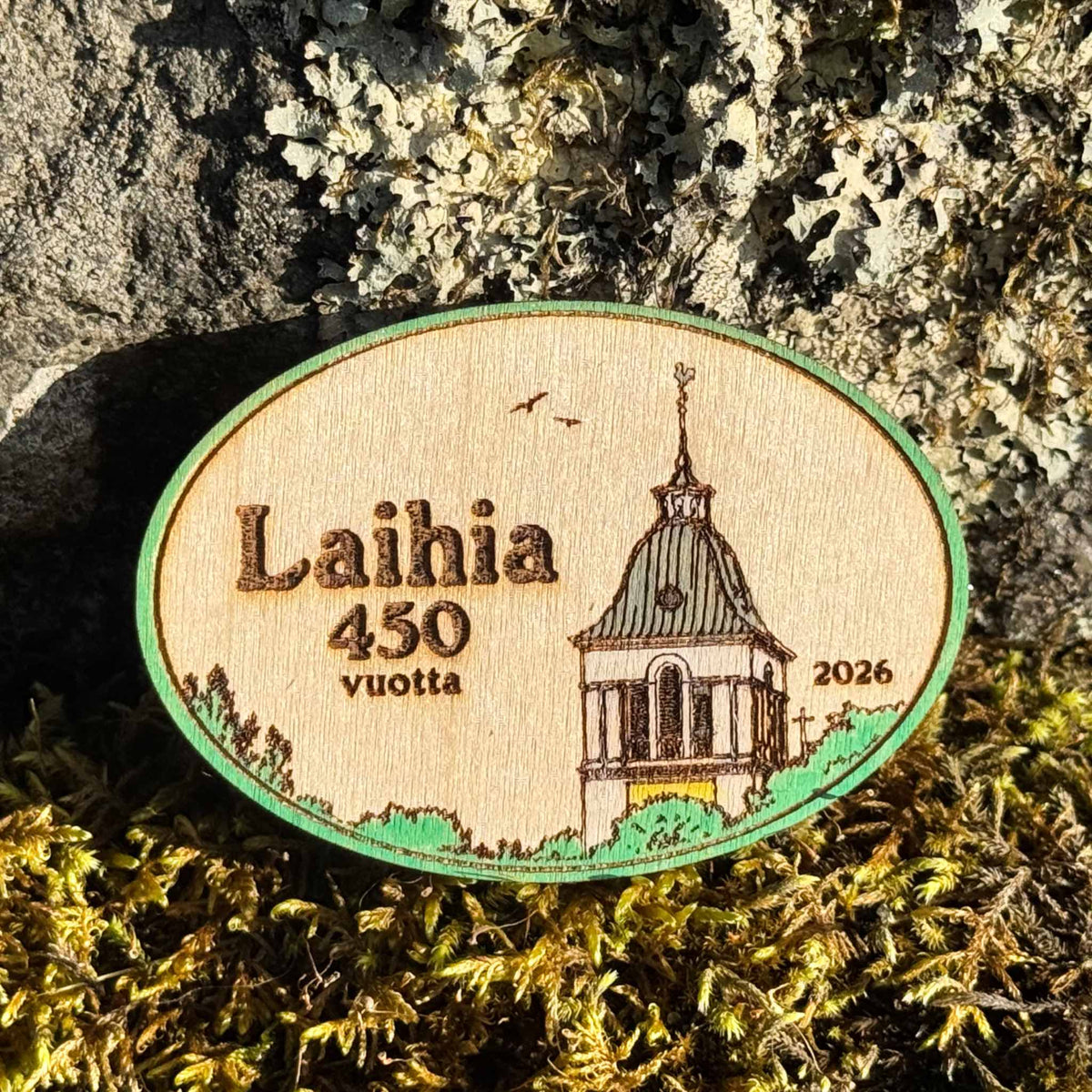 Maalattu soikea Laihia 450 vuotta 2026 -puumagneetti, jossa on kirkkoaihe, vihreä reunus ja värillisiä yksityiskohtia.