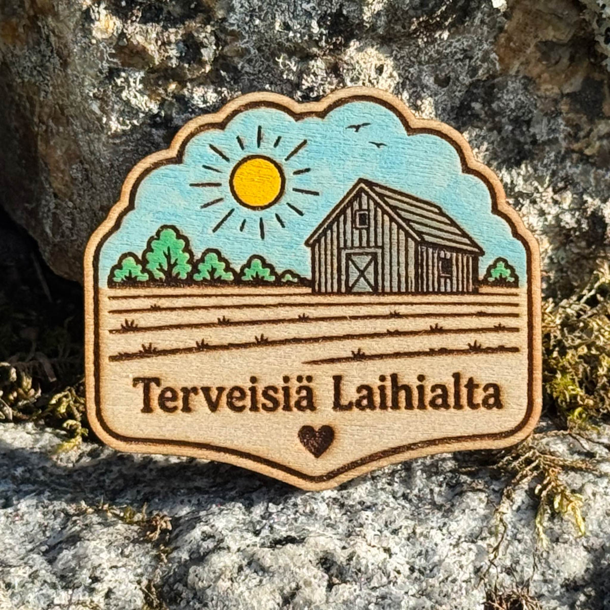 Maalattu puinen Terveisiä Laihialta -magneetti, jossa on aurinko, lato, pelto ja pieni sydän.