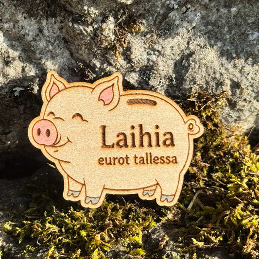Puinen säästöpossun muotoinen jääkaappimagneetti, jossa on vaaleanpunaisia yksityiskohtia ja teksti Laihia eurot tallessa.