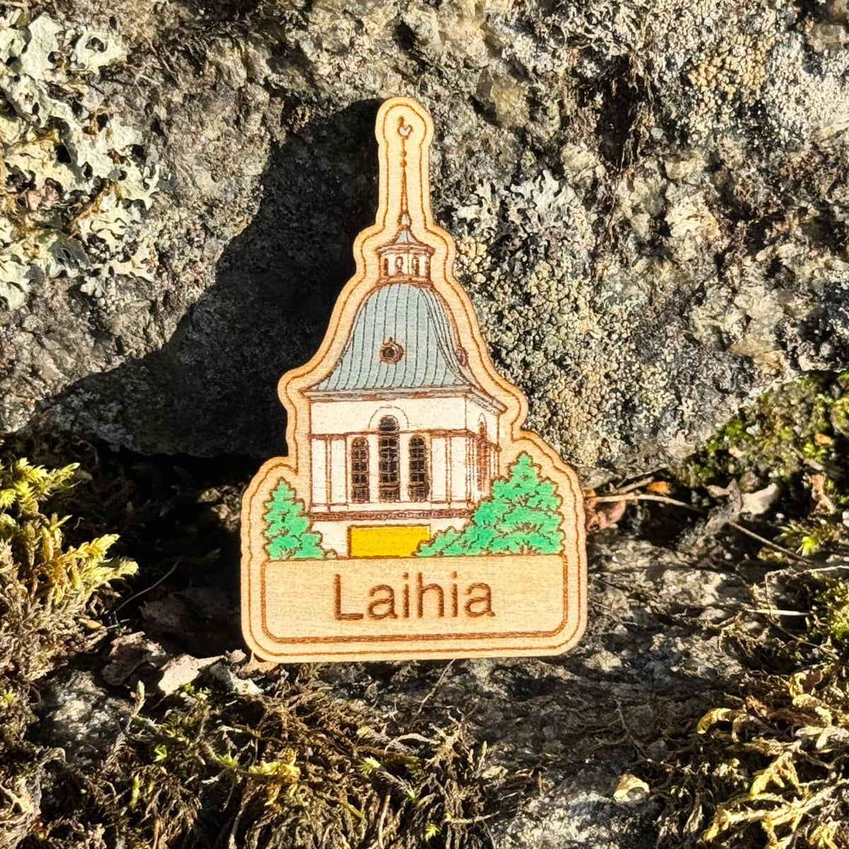 Laihian kirkon tornin muotoinen maalattu puumagneetti, jossa on harmaa katto, vihreitä yksityiskohtia ja Laihia-teksti.