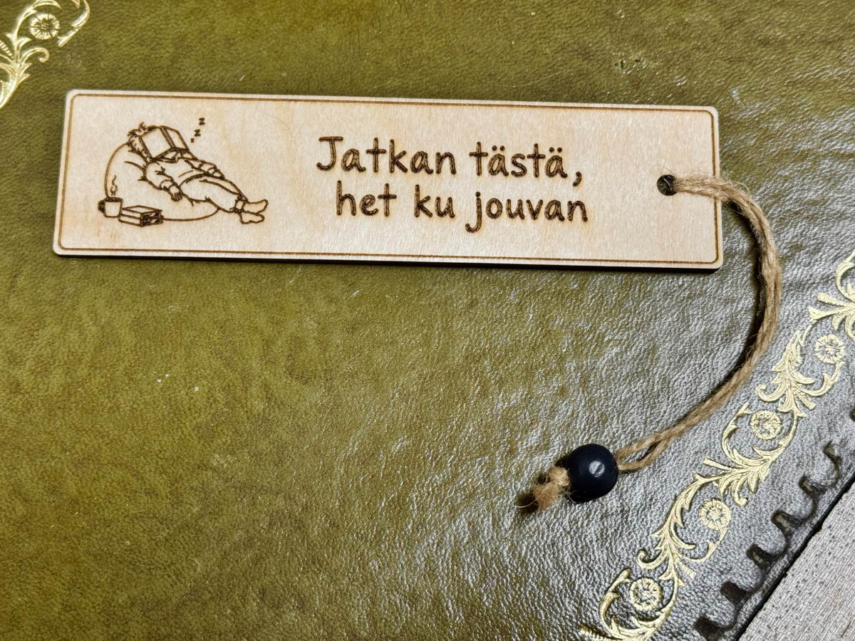 Puinen kirjanmerkki koivuvanerista, teksti Jatkan tästä, het ku jouvan ja levähtävän lukijan kuva – Puukkeli